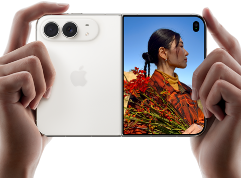 iPhone Duo, i färgen stjärnvit, hålls i två händer i stående läge, utfälld, den vänstra panelen visar 48 MP Fusion-dubbelkameran på baksidan, den högra panelen visar en person som blir fotograferad på den yttre skärmen, personen kan se sitt ansikte medan bilden tas med Duo Preview