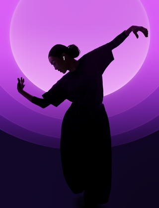 En person som dansar med AirPods 5 i öronen mot en bakgrund i olika färger