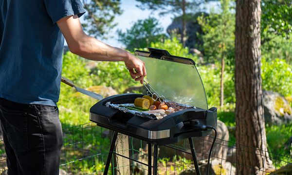 En man förbereder mat och grillar på elektrisk grill under en sommardag