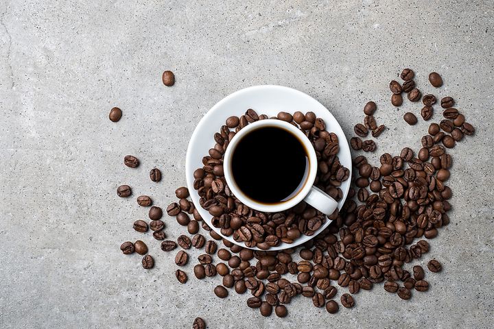 Coffee cup with beans scattered around it on a grey table top