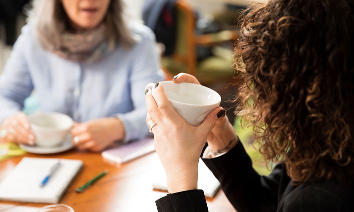 Två kvinnor sitter vid ett bord och dricker kaffe medan de arbetar