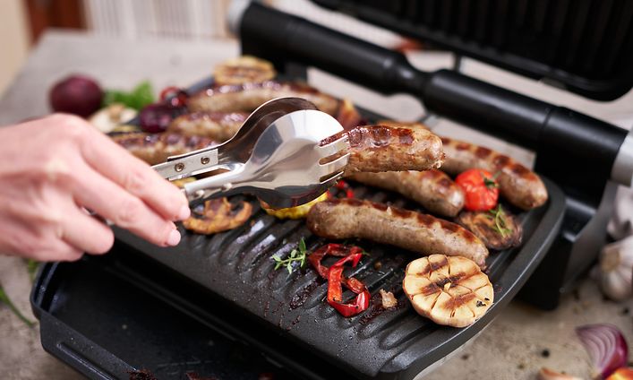 Man grilling sausages and vegetables on electric grill